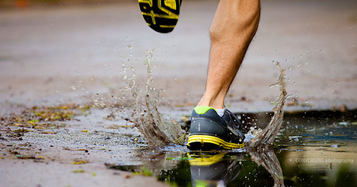 Close-up of a runner's foot in yellow running shoes splashing through a rain puddle — athletic performance recovery and sports therapy at Innovation Wellness in Early, Texas